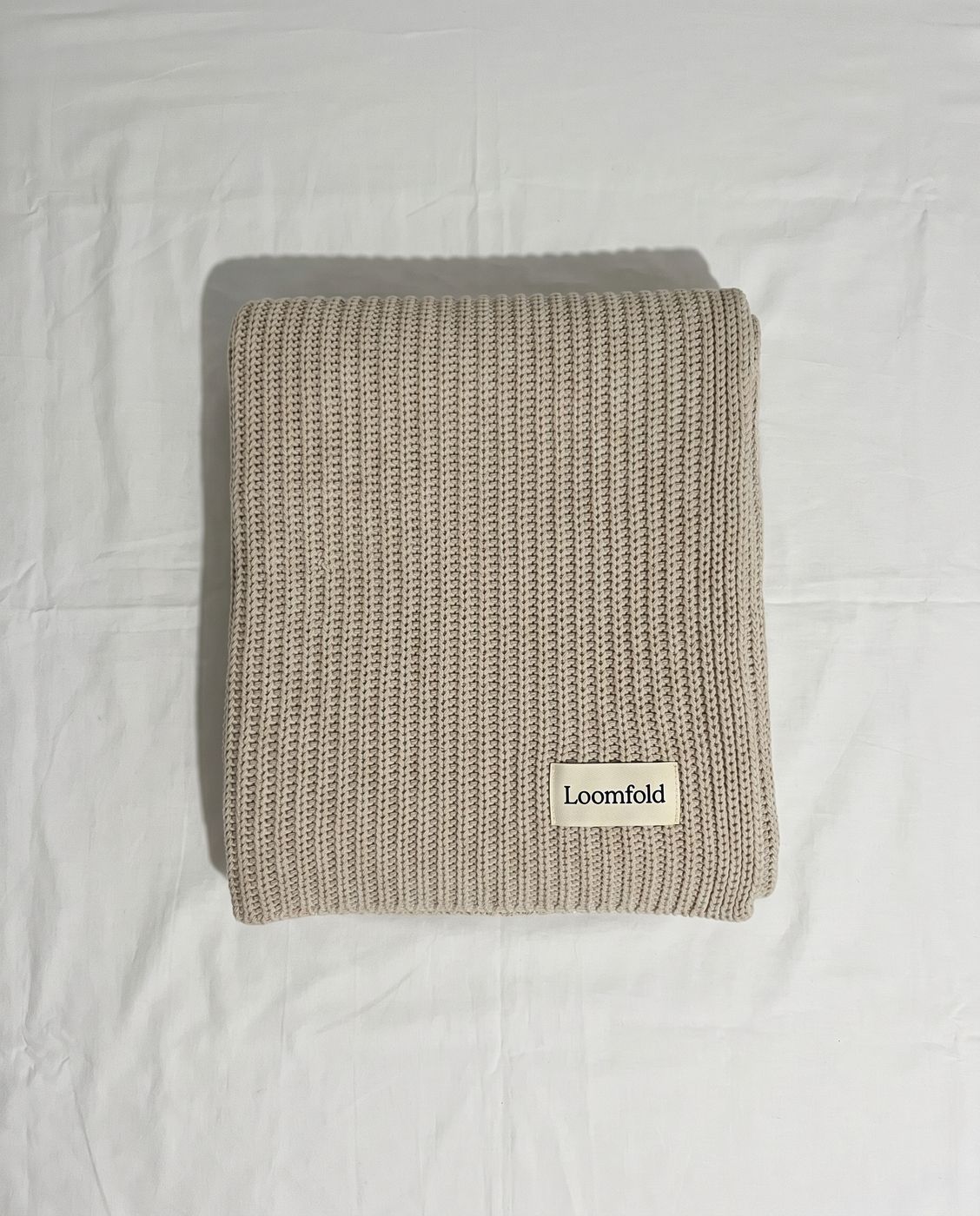 A seller's own phone photo of a folded Loomfold knitted throw on a sheet